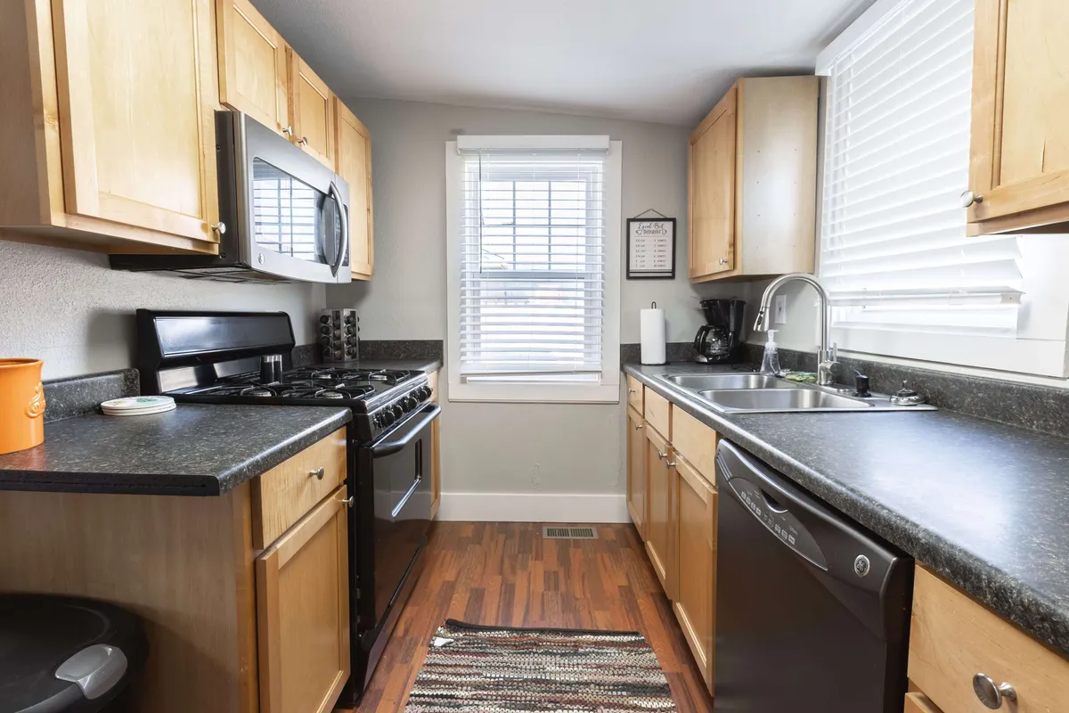 This image presents a cozy and functional kitchen, showcasing modern appliances, generous countertop space, a window for natural light, and a homey rug. The scene evokes a welcoming environment suitable for both cooking and gathering.