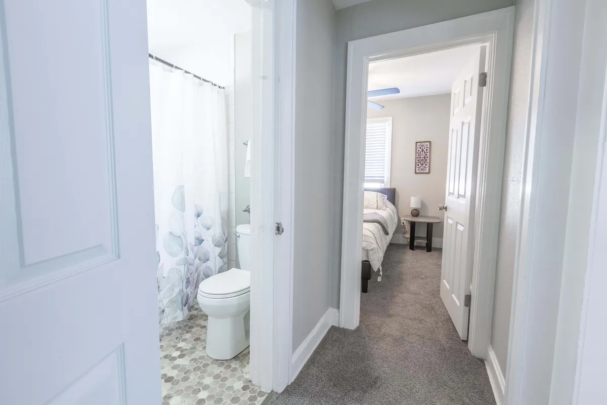 This image offers a view through a doorway that connects different parts of the home, highlighting the entrance to both the bathroom and bedroom. The textured flooring and light-colored walls evoke a sense of flow and transition within the space, inviting thoughts of entering or leaving for an outing.