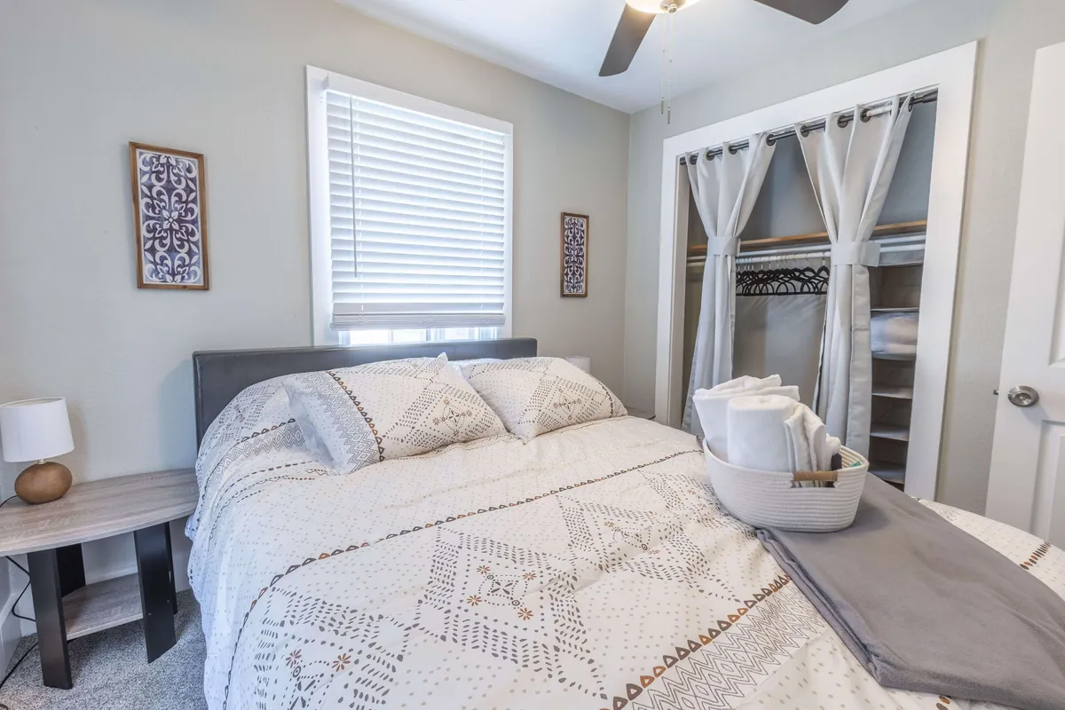 A warmly lit bedroom featuring a comfortable bed with plush linens, a nightstand, decorative wall art, and a spacious closet. The soft natural light emphasizes the cozy reading nook and ample storage, creating an inviting space for relaxation.