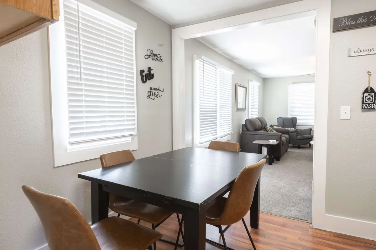 A charming dining area is shown, featuring a welcoming dining table, decorative wall signs, and generous natural light from a nearby window. The setting feels intimate and ideal for family meals or friendly gatherings.