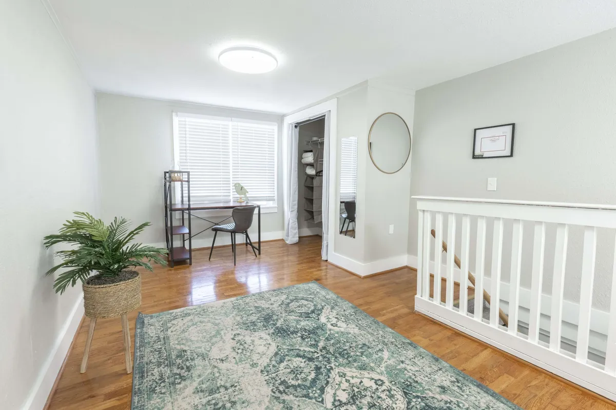 A serene interior space showcasing a desk and chair, accented by a lush green plant, stylish area rug, and a mirror. The layout offers a peaceful atmosphere suitable for unwinding, casual conversation, or quiet solo moments.